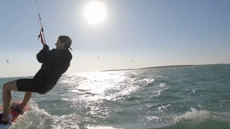 Kiter v protisvětle těsně u kamery, za ním slunce a další kity